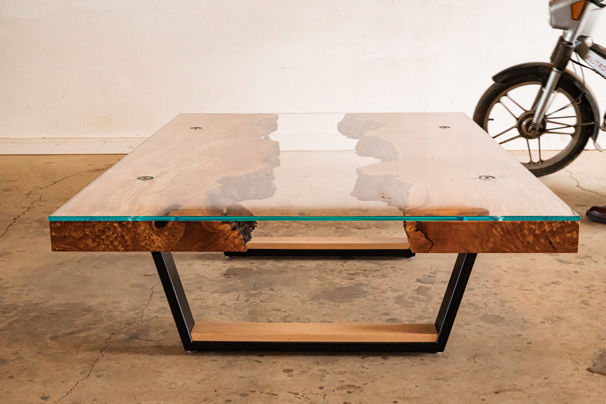 A coffee table crafted from burled maple wood with the live edges facing the center. Glass is set on top of this table complete with a metal base. The wood was finished with Rubio Monocoat hardwax oil wood finish.