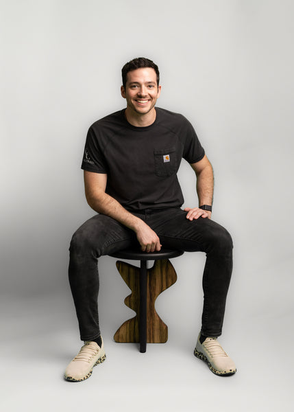 A man is sitting on a side table made from white oak and black limba wood. 