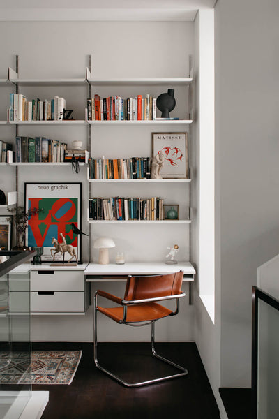 A mid-century modern inspired chair sits adjacent to a bookshelf with a built in desk and drawers. 