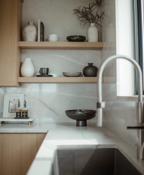 White oak floating shelves in a kitchen made entirely from white oak. The shelves are styled with various vases, books, and other elements. 