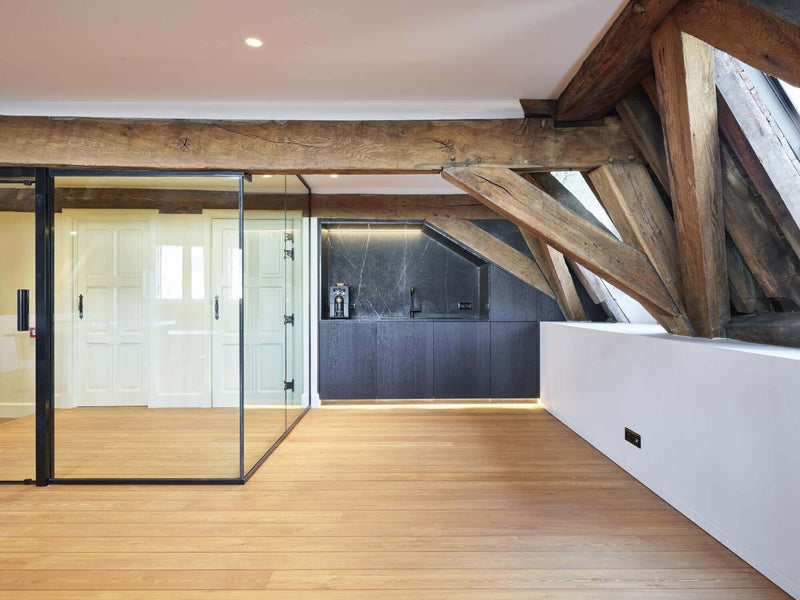 Office space with exposed wood beams, hardwood flooring and a glass rooms.